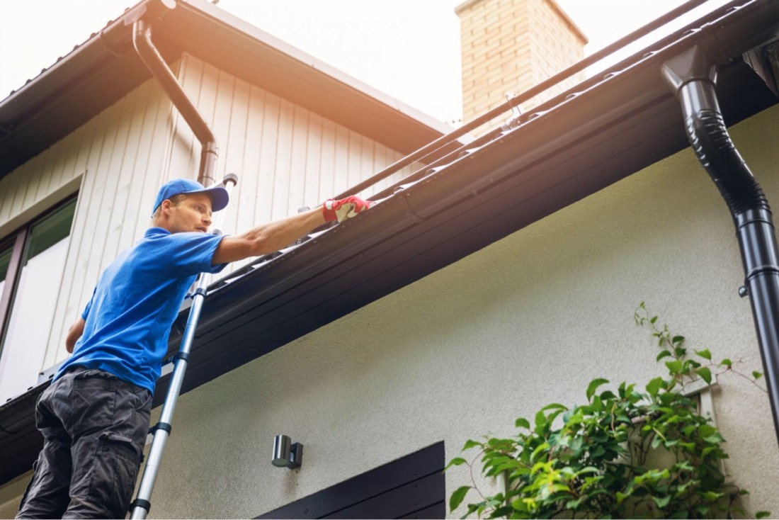 Technician cleaning and servicing gutters from a ladder